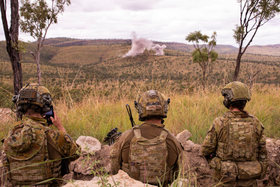 A scout team observing from a hide, one soldier on the radio.