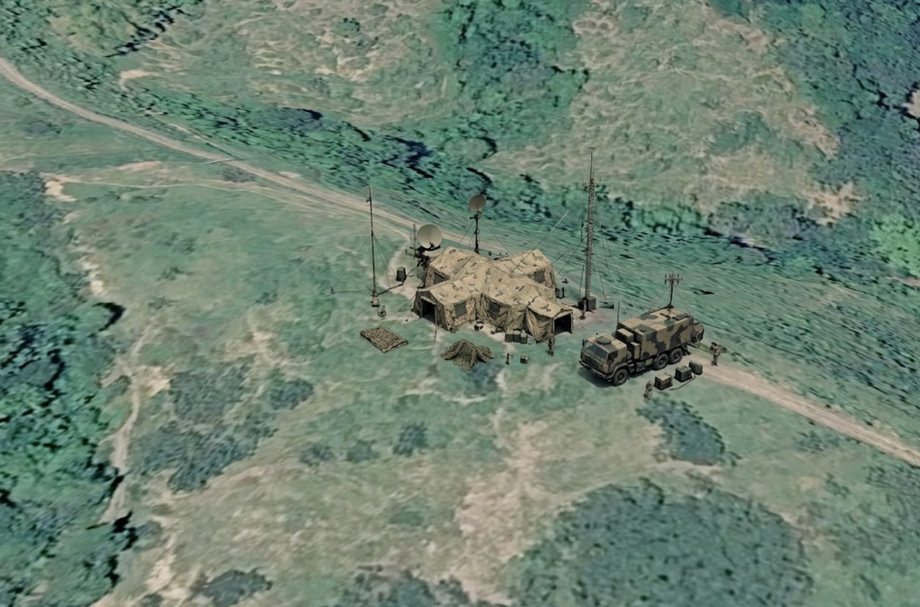 Oblique sensor view of the enemy command post before the attack. Three connected tents stand in a clearing beside a track, with two satellite dishes and a communications mast alongside, and a camouflaged command vehicle parked on the track to the east.